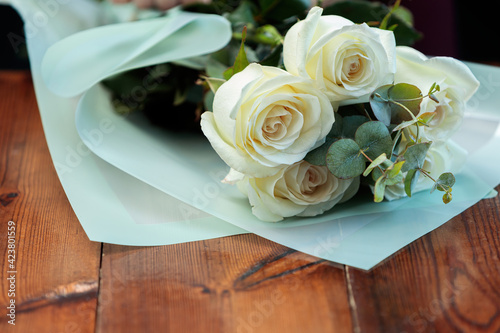 A bouquet of white roses in paper packaging lies on a wooden table.