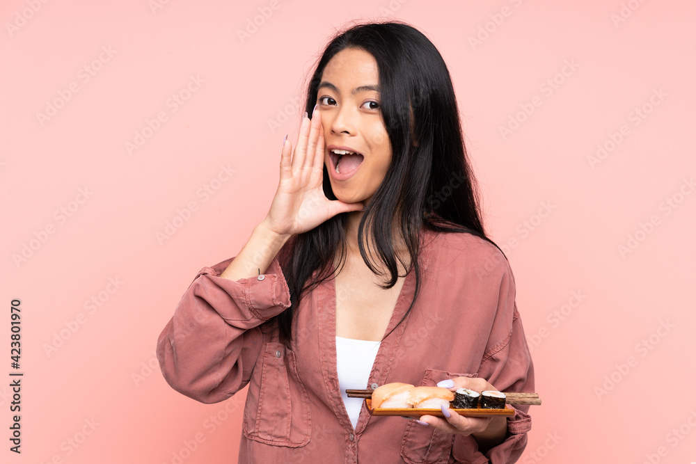 Teenager Asian girl eating sushi isolated on pink background shouting with mouth wide open Teenager Asian girl eating sushi isolated on pink background shouting with mouth wide open
