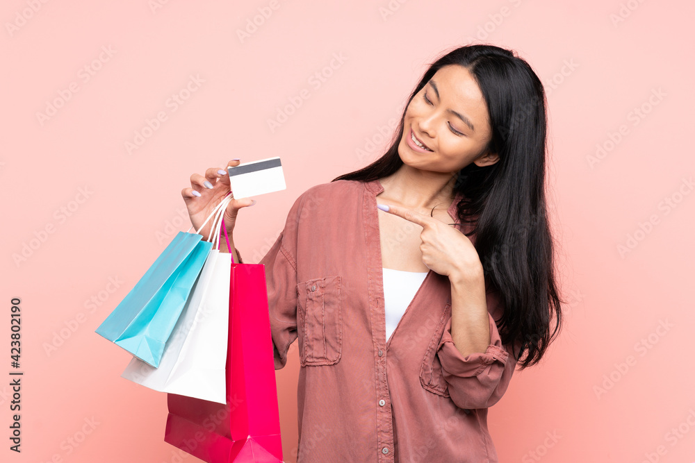 Teenager Chinese girl isolated on pink background holding shopping bags and a credit card Teenager Chinese girl isolated on pink background holding shopping bags and a credit card