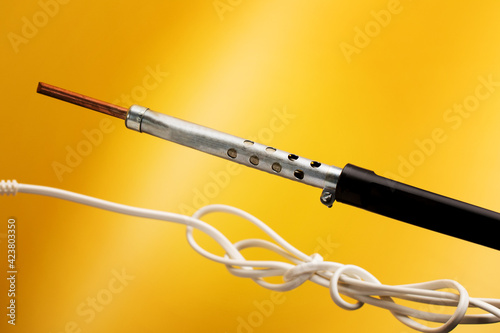 Soldering iron with black plastic handle isolated on yellow background.