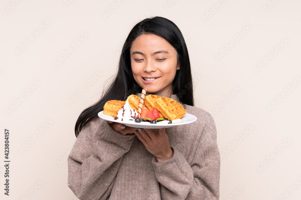 Teenager Asian girl holding waffles isolated on beige background Teenager Asian girl holding waffles isolated on beige background