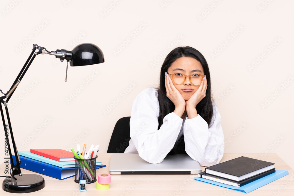 Student asian girl in a workplace with a laptop isolated on beige background Student asian girl in a workplace with a laptop isolated on beige background