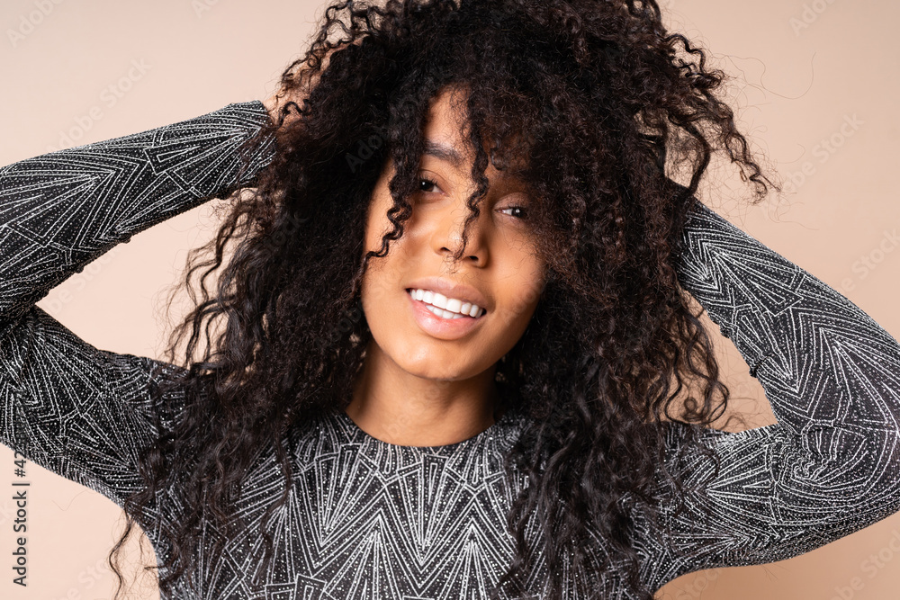 Close up portrait of laufhing woman with brown skin and african hairstyle in shiny party dress posing over beige background.