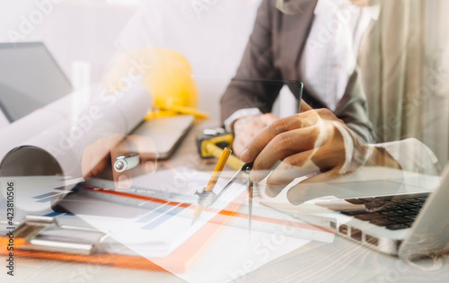 Two colleagues discussing data working and tablet, laptop with on on architectural project at construction site at desk in office