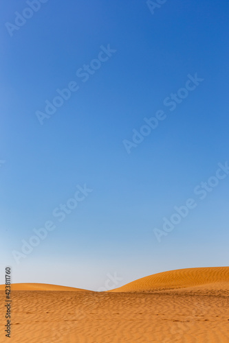 Simple minimalist desert landscape with golden sand dunes, low horizon, crystal blue sky, copy space, background.