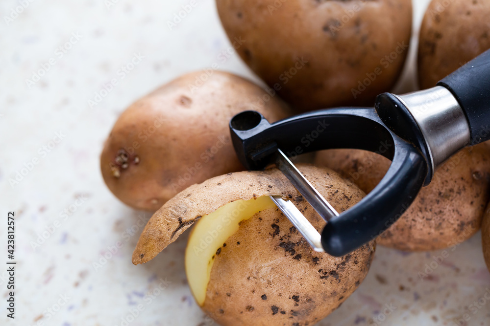Several organic potatoes and a potato peeler on the table. Made in natural light, soft shadows.