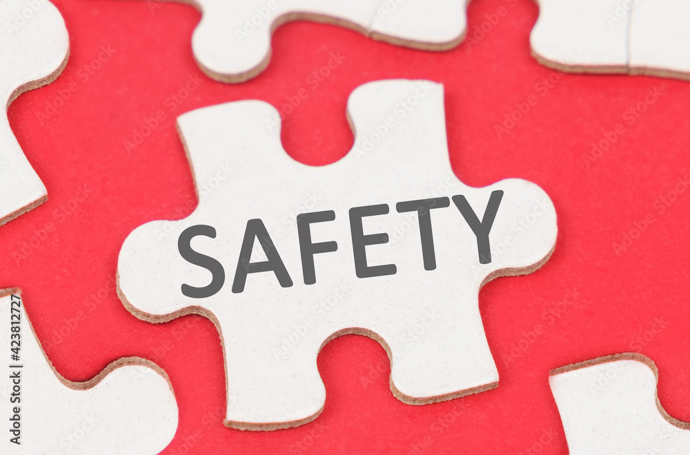 On a red background, among white puzzles lies a puzzle with the inscription - SAFETY On a red background, among white puzzles lies a puzzle with the inscription - SAFETY