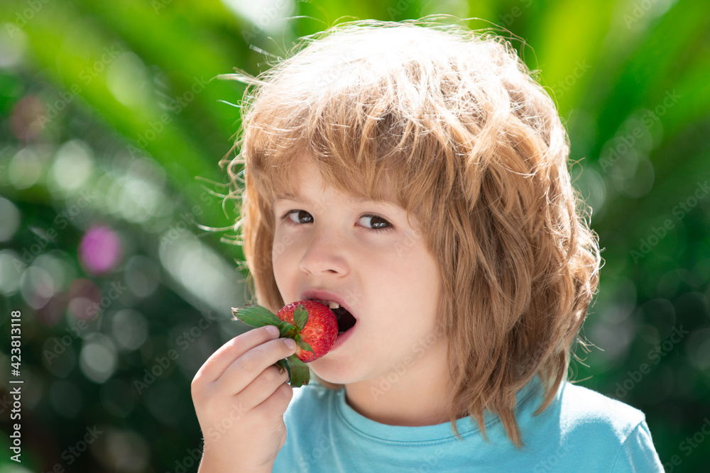 Healthy kids food. Adorable kid eating strawberry on green spring background. Close up kids happy face.