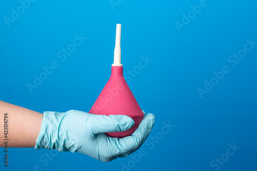 Enema in the hand of a nurse on a blue background.