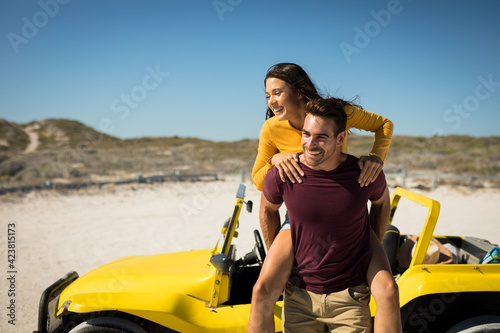 Happy caucasian couple next to beach buggy by the sea piggybacking