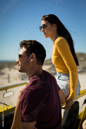 Happy caucasian couple in beach buggy by the sea looking ahead wearing sunglasses