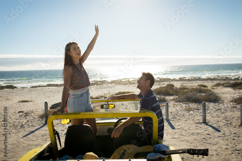 Happy caucasian couple in beach buggy by the sea smiling
