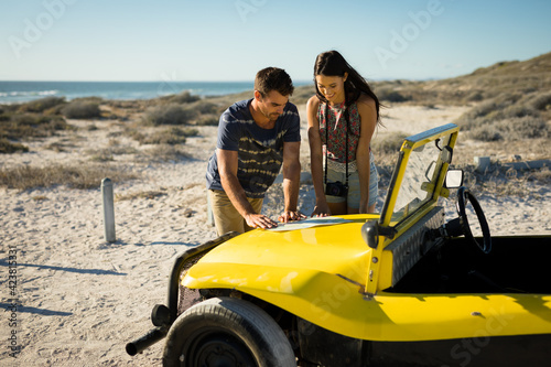 Happy caucasian couple reading roadmap on beach buggy by the sea