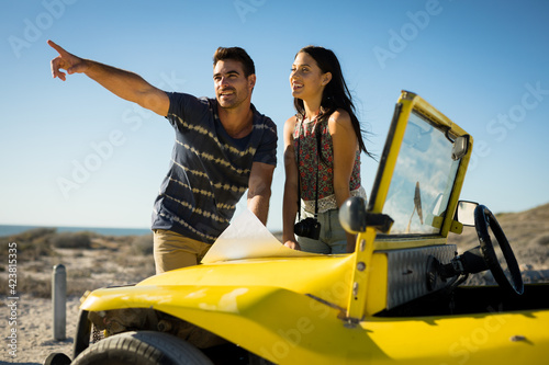 Happy caucasian couple pointing and reading roadmap on beach buggy by the sea