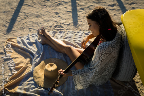 Happy caucasian woman sitting on beach by the sea playing guitar