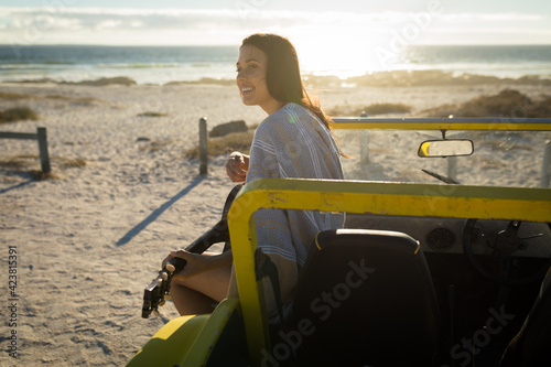 Happy caucasian woman sitting on beach buggy by the sea playing guitar
