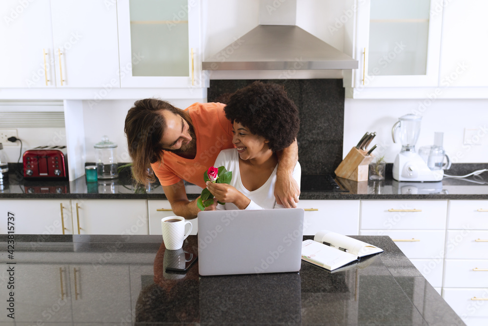 Happy diverse couple sitting in kitchen a man giving her flowers