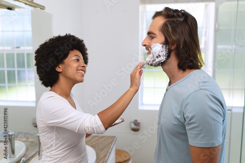 Diverse couple standing in bathroom applying shaving cream