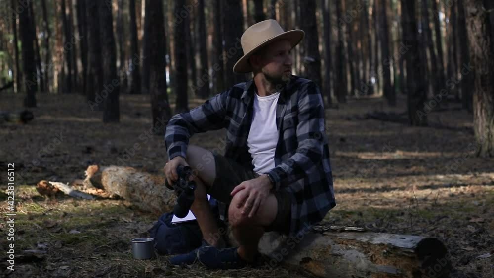Young man resting on a log and looking through binoculars while hiking Young man resting on a log and looking through binoculars while hiking