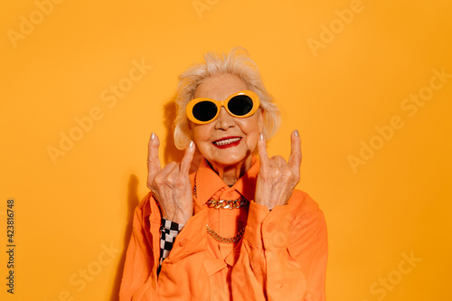 Woman standing over isolated yellow background while doing rock symbol