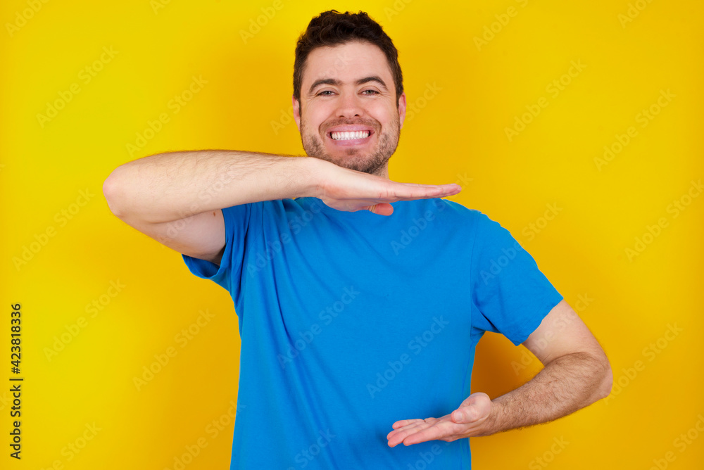 young handsome caucasian man wearing blue t-shirt against yellow background gesturing with hands showing big and large size sign, measure symbol. Smiling looking at the camera. young handsome caucasian man wearing blue t-shirt against yellow background gesturing with hands showing big and large size sign, measure symbol. Smiling looking at the camera.