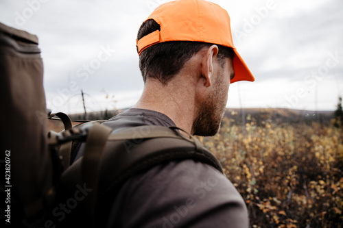 a man walking in the bush alaska while hunting while wearing an orange hunting hat for hunting safety when hunting for game