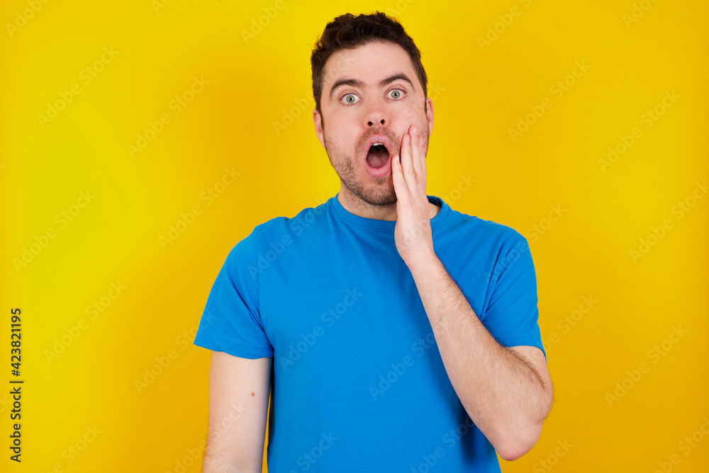 young handsome caucasian man wearing blue t-shirt against yellow background very happy and excited doing winner gesture with arms raised, smiling and screaming for success. Celebration concept. young handsome caucasian man wearing blue t-shirt against yellow background very happy and excited doing winner gesture with arms raised, smiling and screaming for success. Celebration concept.