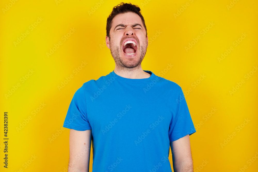 young handsome caucasian man wearing blue t-shirt against yellow background suffering from strong headache desperate and stressed because of overwork. Depression and pain concept. young handsome caucasian man wearing blue t-shirt against yellow background suffering from strong headache desperate and stressed because of overwork. Depression and pain concept.
