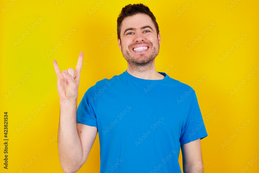 young handsome caucasian man wearing blue t-shirt against yellow background smiling swearing with hand on chest and fingers up, making a loyalty promise oath. young handsome caucasian man wearing blue t-shirt against yellow background smiling swearing with hand on chest and fingers up, making a loyalty promise oath.