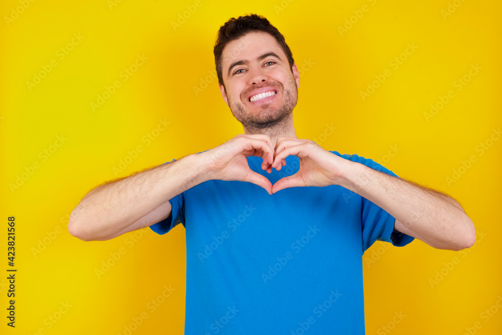 young handsome caucasian man wearing blue t-shirt against yellow background looking at the camera blowing a kiss with hand on air being lovely and sexy. Love expression. young handsome caucasian man wearing blue t-shirt against yellow background looking at the camera blowing a kiss with hand on air being lovely and sexy. Love expression.