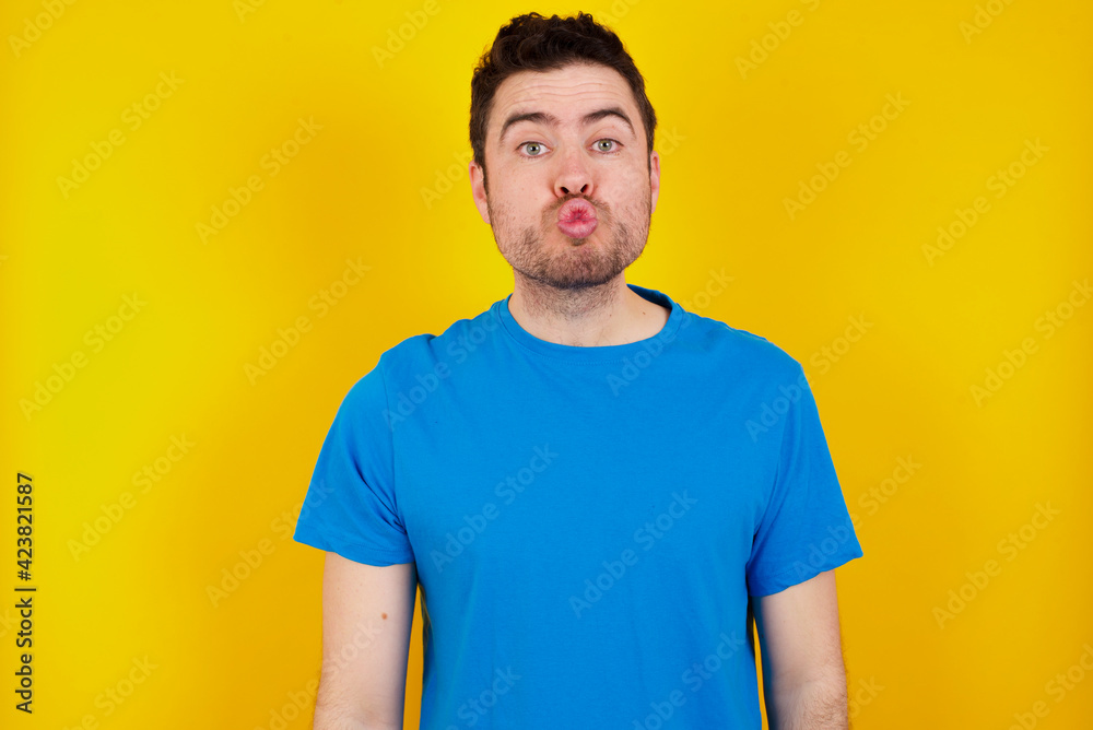 young handsome caucasian man wearing blue t-shirt against yellow background smiling in love doing heart symbol shape with hands. Romantic concept. young handsome caucasian man wearing blue t-shirt against yellow background smiling in love doing heart symbol shape with hands. Romantic concept.