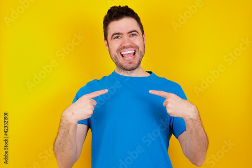 Embarrassed young handsome caucasian man wearing blue t-shirt against yellow background with shocked expression, expresses great amazement, Puzzled model poses indoor