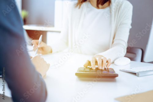 Accountant checking financial statement or counting by calculator income for tax form, hands closeup. Business woman sitting and working with colleague at the desk in office. Tax and Audit concept