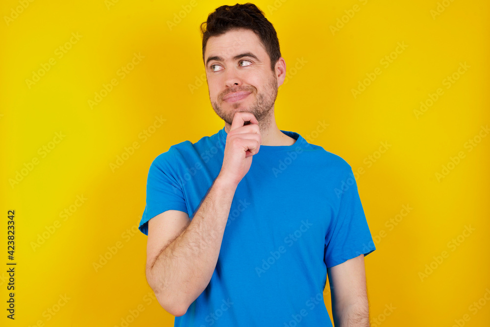 Shocked embarrassed young handsome caucasian man wearing blue t-shirt against yellow background keeps mouth widely opened. Hears unbelievable novelty stares in stupor