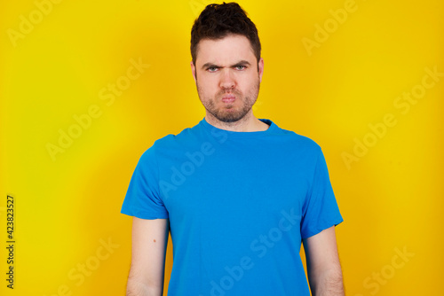 young handsome caucasian man wearing blue t-shirt against yellow background stares aside with wondered expression has speechless expression. Embarrassed model looks in surprise