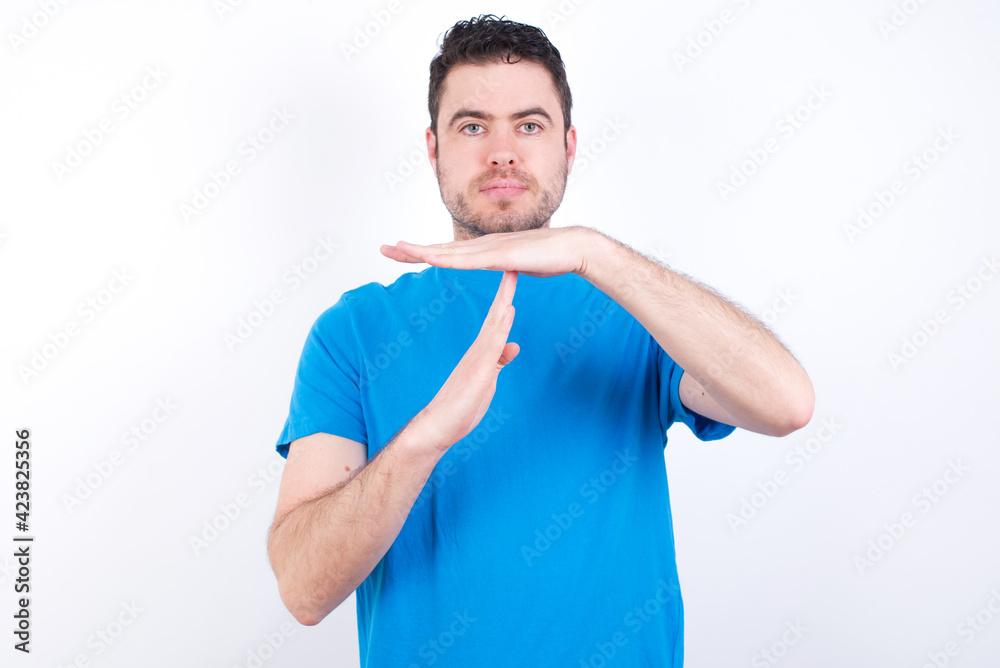 young handsome caucasian man wearing blue t-shirt against white background being upset showing a timeout gesture, needs stop, asks time for rest after hard work, demonstrates break hand sign young handsome caucasian man wearing blue t-shirt against white background being upset showing a timeout gesture, needs stop, asks time for rest after hard work, demonstrates break hand sign