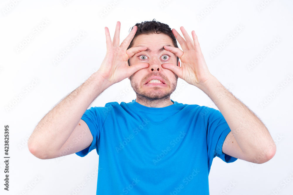 young handsome caucasian man wearing blue t-shirt against white background keeping eyes opened to find a success opportunity. young handsome caucasian man wearing blue t-shirt against white background keeping eyes opened to find a success opportunity.