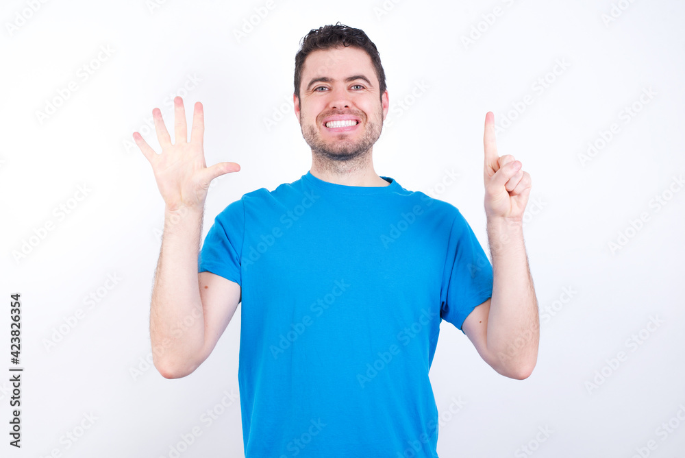 young handsome caucasian man wearing blue t-shirt against white background showing and pointing up with fingers number six while smiling confident and happy. young handsome caucasian man wearing blue t-shirt against white background showing and pointing up with fingers number six while smiling confident and happy.