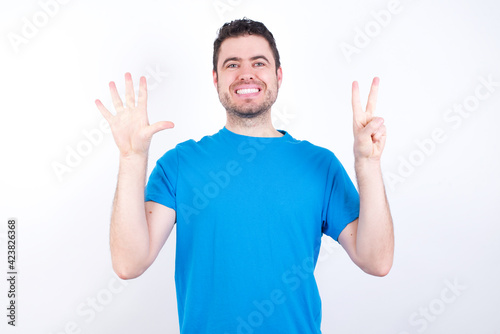 young handsome caucasian man wearing blue t-shirt against white background showing and pointing up with fingers number seven while smiling confident and happy.