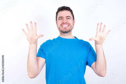 young handsome caucasian man wearing blue t-shirt against white background showing and pointing up with fingers number ten while smiling confident and happy.