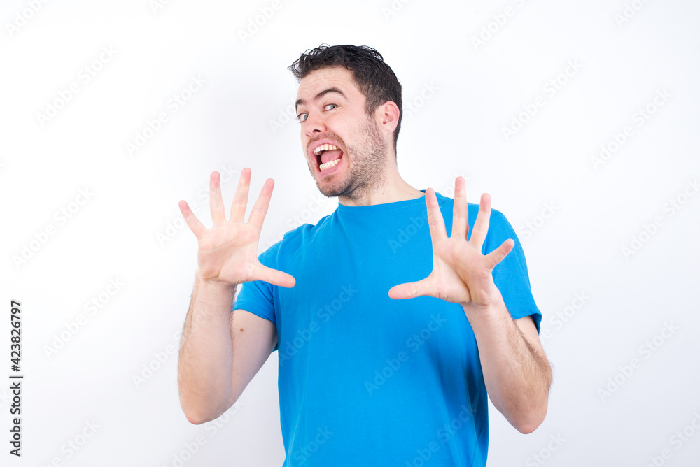 young handsome caucasian man wearing blue t-shirt against white background afraid and terrified with fear expression stop gesture with hands, shouting in shock. Panic concept. young handsome caucasian man wearing blue t-shirt against white background afraid and terrified with fear expression stop gesture with hands, shouting in shock. Panic concept.