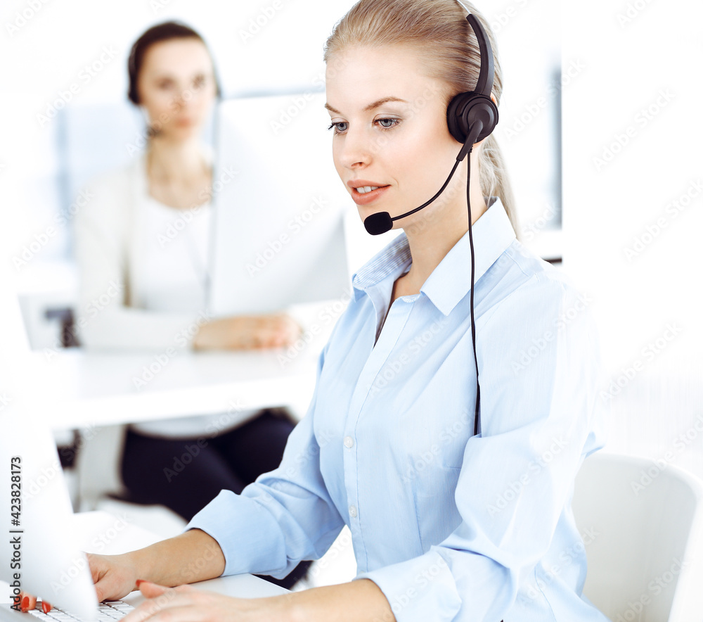 Blond woman call operator is using computer and headset for consulting clients online. Group of diverse people working as customer service occupation. Business concept Blond woman call operator is using computer and headset for consulting clients online. Group of diverse people working as customer service occupation. Business concept