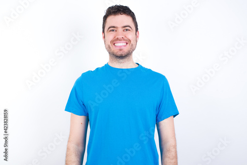 young handsome caucasian man wearing white t-shirt against white background with nice beaming smile pleased expression. Positive emotions concept