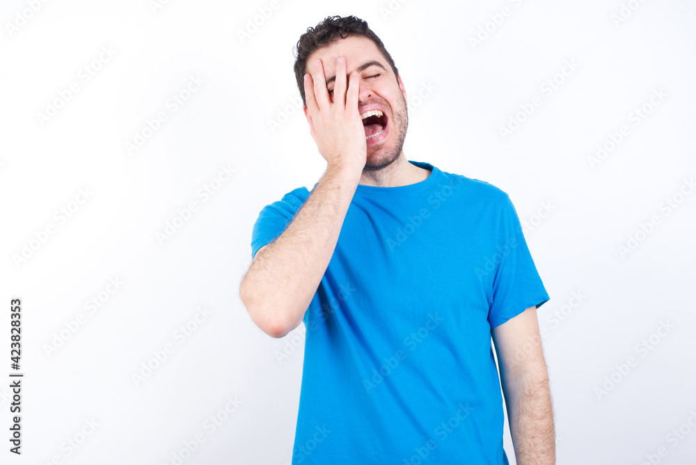 young handsome caucasian man wearing white t-shirt against white background makes face palm and smiles broadly, giggles positively hears funny joke poses young handsome caucasian man wearing white t-shirt against white background makes face palm and smiles broadly, giggles positively hears funny joke poses
