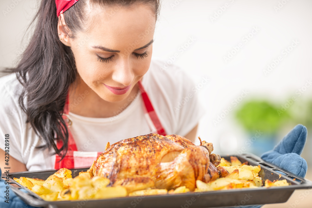 Young housewife smells freshly baked chicken and potatoes from a tray Young housewife smells freshly baked chicken and potatoes from a tray