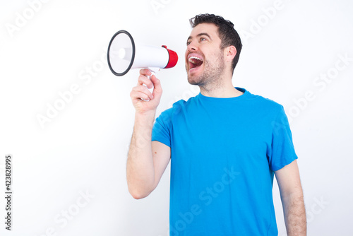 Funny young handsome caucasian man wearing white t-shirt against white background People sincere emotions lifestyle concept. Mock up copy space. Screaming in megaphone.