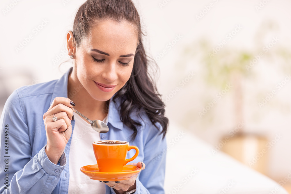 Beautiful woman smells fresh coffee from an orange cup Beautiful woman smells fresh coffee from an orange cup