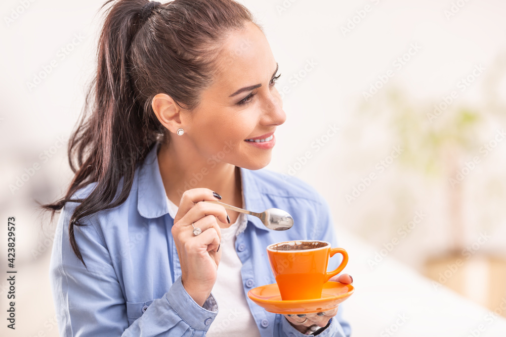 Young woman holds morning coffee in an orange cup and a spoon in her hand Young woman holds morning coffee in an orange cup and a spoon in her hand