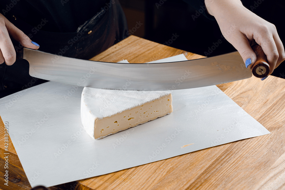 Brie soft white cheese from cow milk. Slicing brie on the wooden table. Organic delicious food Brie soft white cheese from cow milk. Slicing brie on the wooden table. Organic delicious food