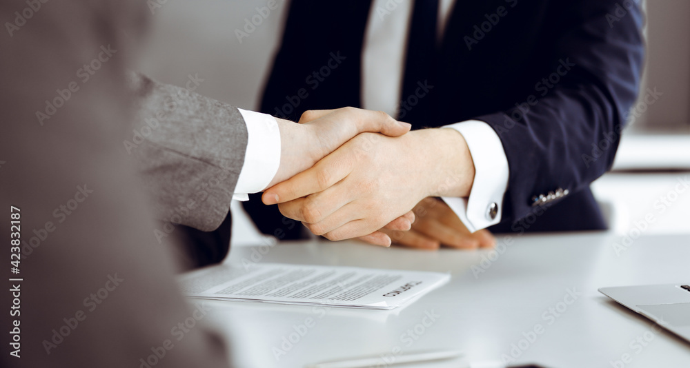 Unknown businessman shaking hands with his colleague or partner above the glass desk in modern office, close-up. Business people group at meeting Unknown businessman shaking hands with his colleague or partner above the glass desk in modern office, close-up. Business people group at meeting